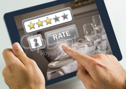 Hand touching tablet with Rate button and review stars in  in restaurant with dinner food