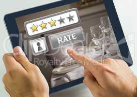 Hand touching tablet with Rate button and review stars in  in restaurant with dinner food