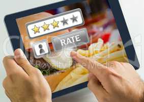 Hand touching tablet with Rate button and review stars in restaurant with burger dinner food
