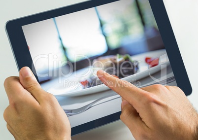 Hand touching tablet in restaurant with dinner food