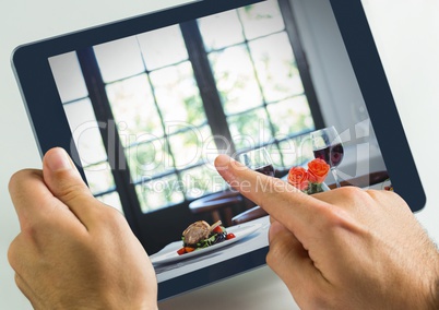 Hand touching tablet with dinner in restaurant