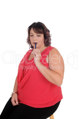 Heavy woman sitting with pen in mouth