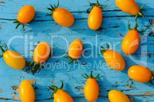 Yellow small tomatoes on blue wooden surface. top view.