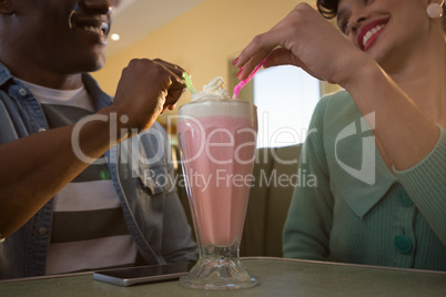 Smiling couple sitting on couch having milkshake in restaurant