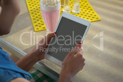 Woman using tablet while having milkshake in the restaurant