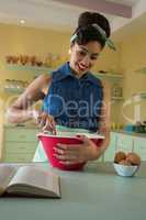 Smiling woman reading recipe while whisking mixture in the kitchen