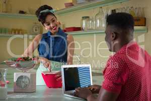 Woman preparing food while man using laptop in kitchen
