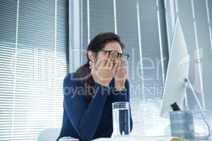 Tired female executive rubbing her eyes at desk