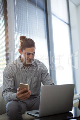 Male executive holding mobile phone while using laptop