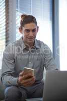 Portrait of male executive holding mobile phone while using laptop