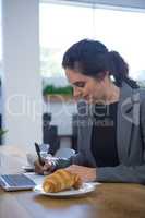 Female executive working at desk while having breakfast