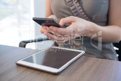 Mid section of female executive using mobile phone at table