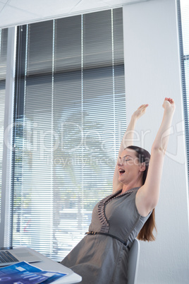 Tired female executive stretching her arms up at desk