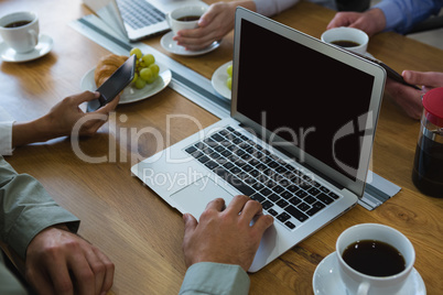 Male executive having coffee while using laptop