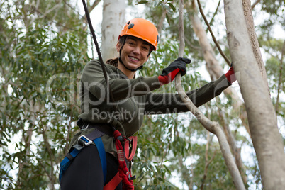 Young smiling woman wearing safety helmet leaning on tree branch in the forest