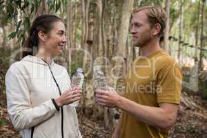 Couple looking at each other holding water bottle in there hands in the forest