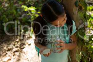 Little girl with backpack looking into jar with plant on a sunny day