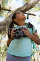 Little girl with backpack holding dslr camera in her hand looking up in the sky on a sunny day