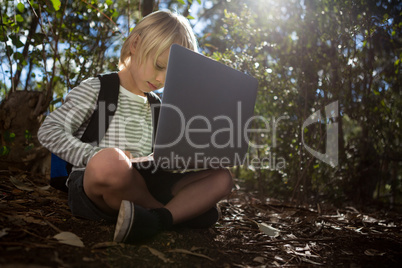 Little girl with a backpack sitting on ground using her laptop