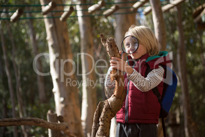 Little girl with backpack looking at wood through magnifying glass