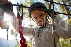 Little girl wearing helmet standing near zip line in the forest