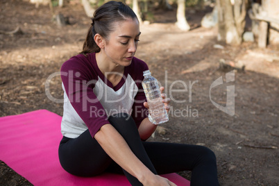 Woman sitting on mat drinking water after exercising