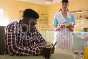 Man using mobile phone while waitress serving breakfast