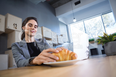 Female executive having croissant at table