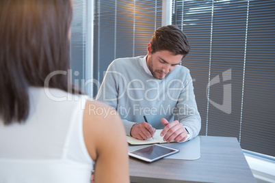 Male executive writing in organizer during meeting