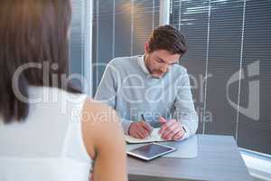 Male executive writing in organizer during meeting