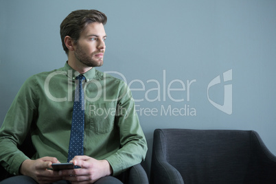 Male executive sitting with mobile phone in waiting area