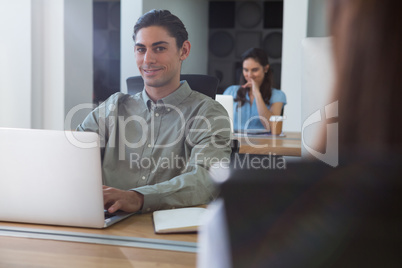 Male executive working on laptop while looking at camera