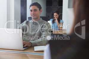 Male executive working on laptop while looking at camera