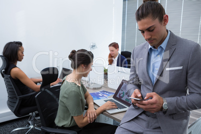 Male executive using mobile phone while colleagues working in background