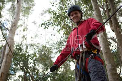 Young hiker man wearing safety helmet holding zip line in the forest during daytime