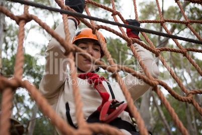 Woman wearing safety helmet climbing on a rope fence in the forest