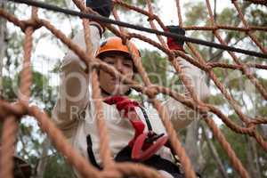 Woman wearing safety helmet climbing on a rope fence in the forest