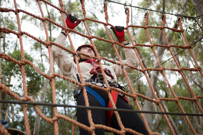 Woman wearing safety helmet climbing on a rope fence
