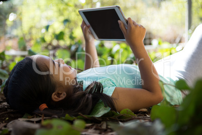 Little girl lying on ground using her tablet on a sunny day