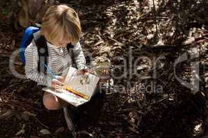 Little girl with backpack sitting on ground writing in notebook