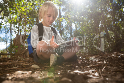 Little girl with backpack sitting on ground using her tablet