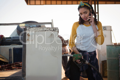 Woman talking on mobile phone while filling petrol in car