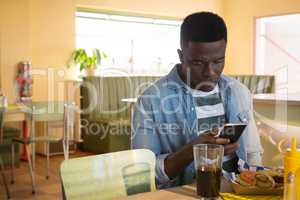 Young man using his mobile phone while having food