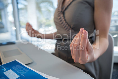 Mid section of female executive performing yoga at desk