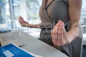 Mid section of female executive performing yoga at desk