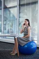 Female executive sitting on exercise ball while talking on mobile phone