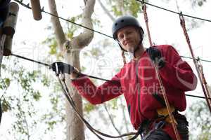 Young man wearing safety helmet crossing zip line in the forest