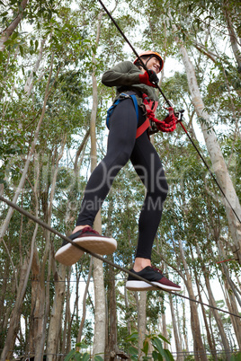 Young smiling woman wearing safety helmet crossing zip line