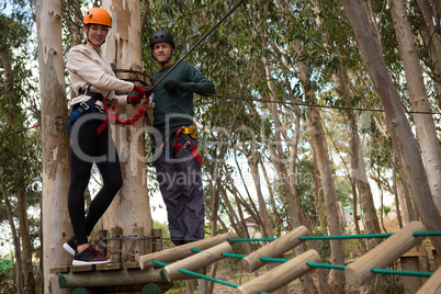 Smiling couple holding zip line cable standing on wooden platform in the forest