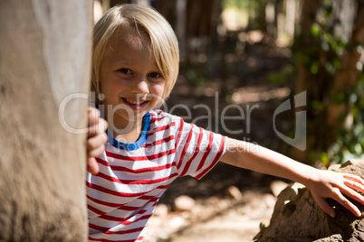 Happy little girl leaning on the tree trunk on a sunny day